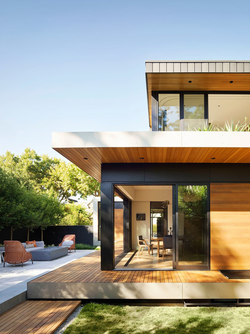 This modern house has sliding glass doors that open the interiors to the yard and entertaining area, that's been furnished with a lounge and freestanding fireplace, as well as an outdoor dining area. #OutdoorSpace #LandscapeDesign #Yard #Backyard #OutdoorLounge #OutdoorDining