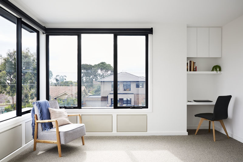 The windows on the second floor of this modern house provide views of the neighborhood, and make this room bright and airy. A desk with a shelf and storage cabinet has been built into a small alcove in the corner of the room. #SmallDesk #Windows #BlackFramedWindows