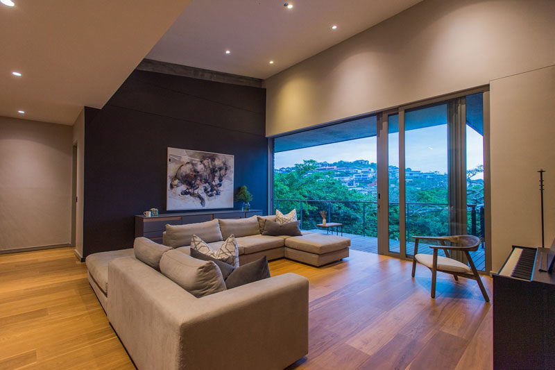 This modern living room features a dark accent wall that highlights the artwork, while sliding glass doors open to a balcony with treetop views. #LivingRoom #DarkAccentWall