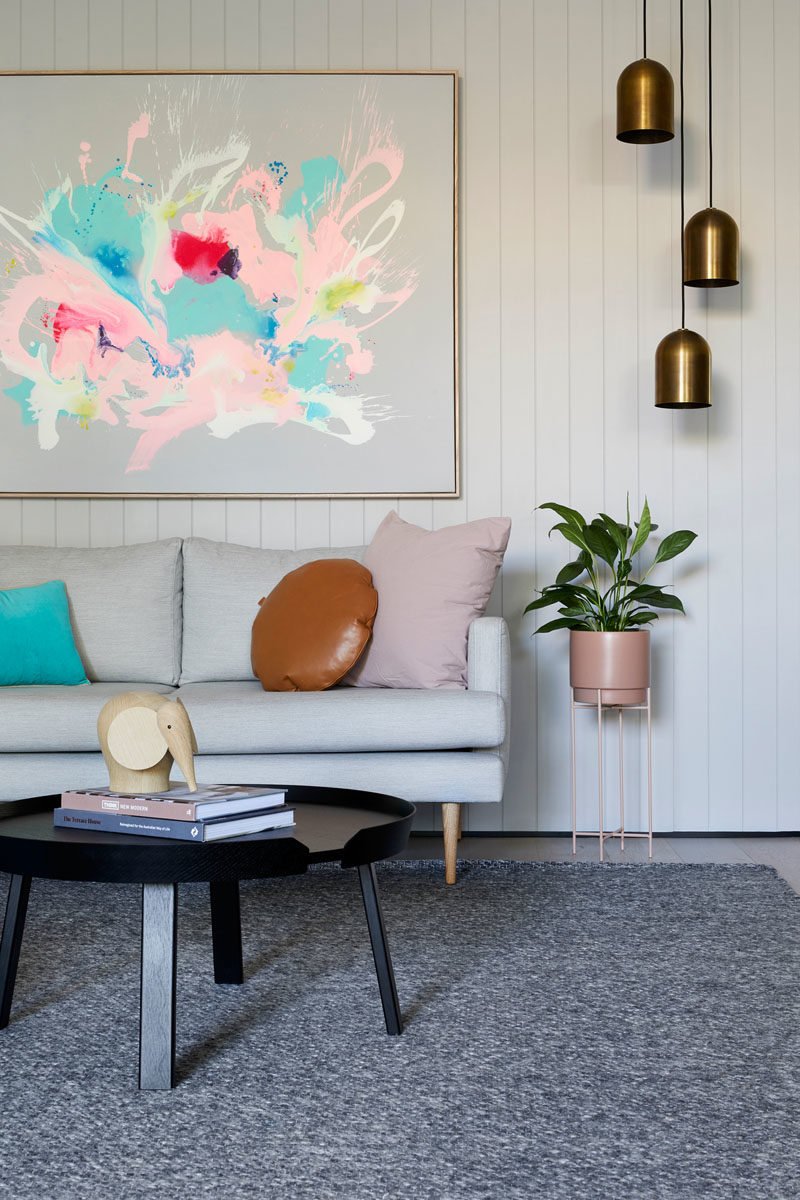 Living Room Ideas -This modern living room takes advantage of the white walls by placing a large colorful abstract art piece above the couch, while three metallic pendant lights hang above a plant on a plant stand. #LivingRoomIdeas #LivingRoom #Decor #InteriorDesign