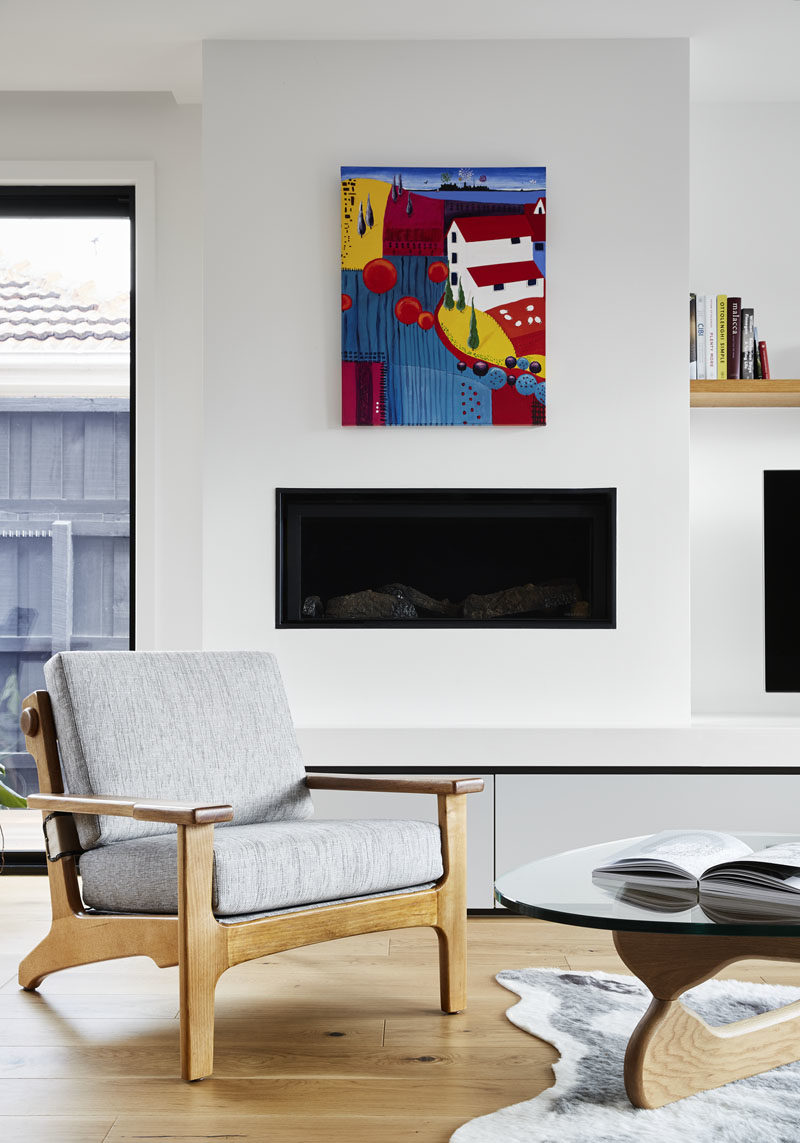 A bright piece of colorful art hangs above a built-in fireplace in this modern living room. #Fireplace #LivingRoom #ModernInteriorDeisgn