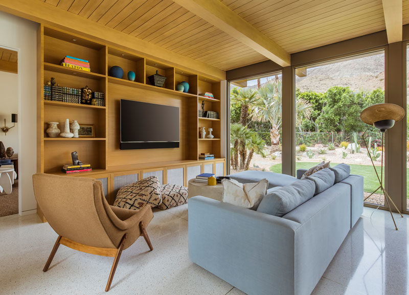 A custom-designed wood shelving unit surrounds the television in this modern living room, while the floor-to-ceiling windows showcase the views outside. #LivingRoom #Shelving