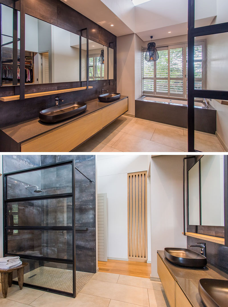 In this modern master bathroom, a long wood floating vanity has plenty of room for two basins, while the built-in bath has been positioned underneath the window, and the shower is separated from the rest of the bathroom by a black-framed glass wall. #ModernBathroom #BathroomIdeas #BuiltInBathtub