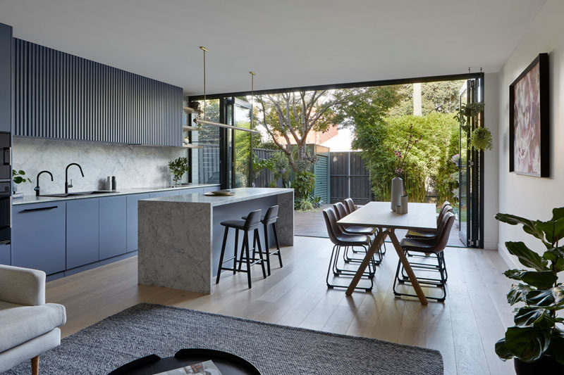 The rear of this modern house is organized in an open plan layout, with the living room, dining area, and kitchen all sharing the same space. Folding glass doors connect the interior with the yard. #InteriorDesign #OpenPlanLayout