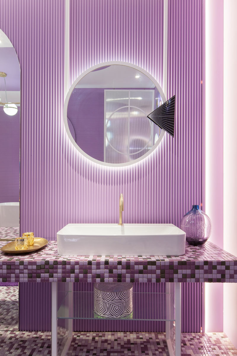 Bathroom Ideas - A mosaic vanity in shades of purple sits below aluminum mirrors that are backlit to provide a soft glow and highlight the textured wall. #BathroomIdeas #BathroomDesign #PurpleBathroom #PurpleTiles