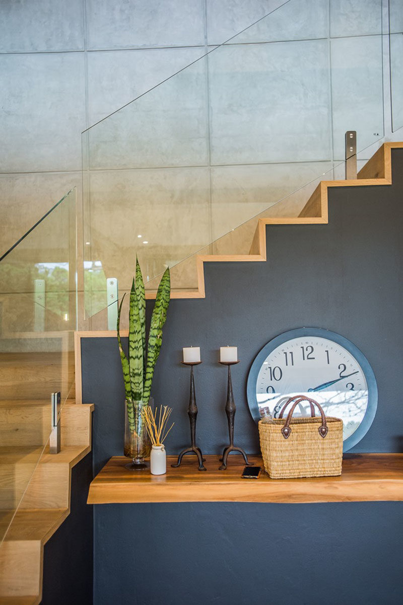 This modern house has stairs with wood treads and glass railings, while a live-edge shelf adds a more natural touch to the interior. #LiveEdgeShelf #ModernStairs