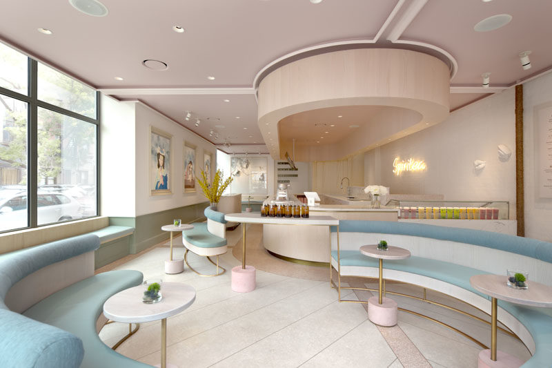 The modern gallery-like interior of this tea store, has light pink and blue accents, and features built-in benches that line the windows and walls. #TeaStore #InteriorDesign #Interiors #Cafe #Seating