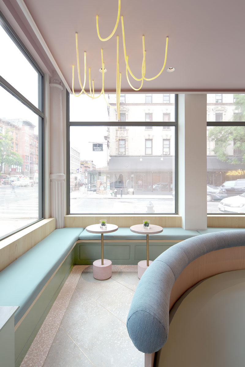 The modern gallery-like interior of this tea store, has light pink and blue accents, and features built-in benches that line the windows and walls. #TeaStore #InteriorDesign #Interiors #Cafe #Seating