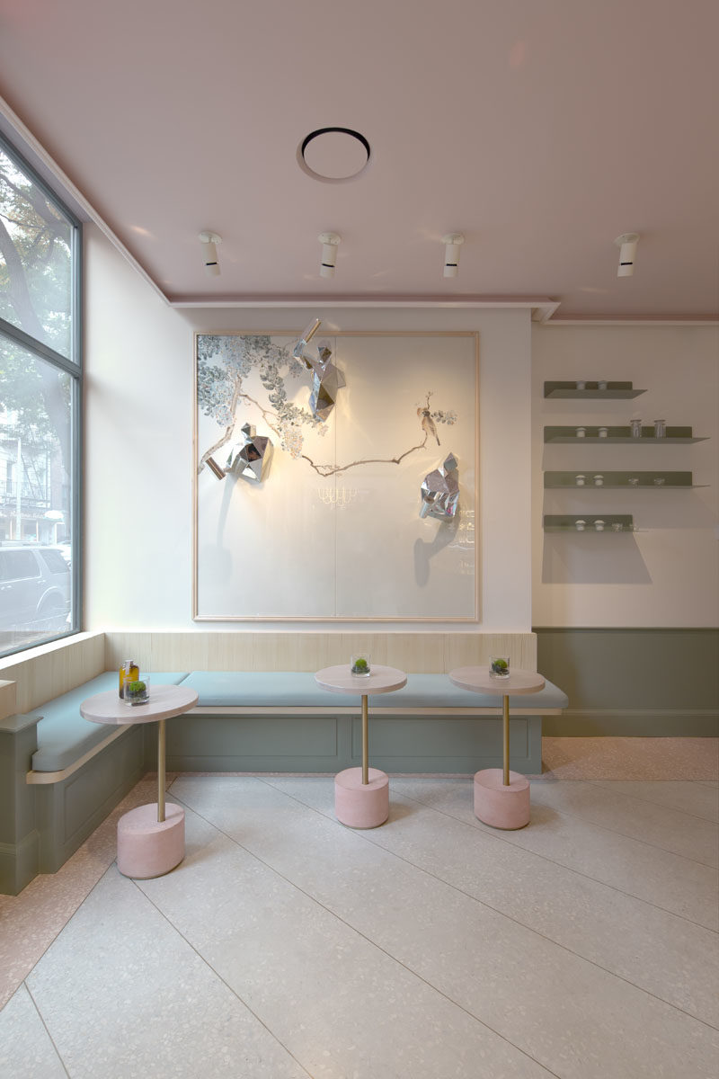 The modern gallery-like interior of this tea store, has light pink and blue accents, and features built-in benches that line the windows and walls. #TeaStore #InteriorDesign #Interiors #Cafe #Seating