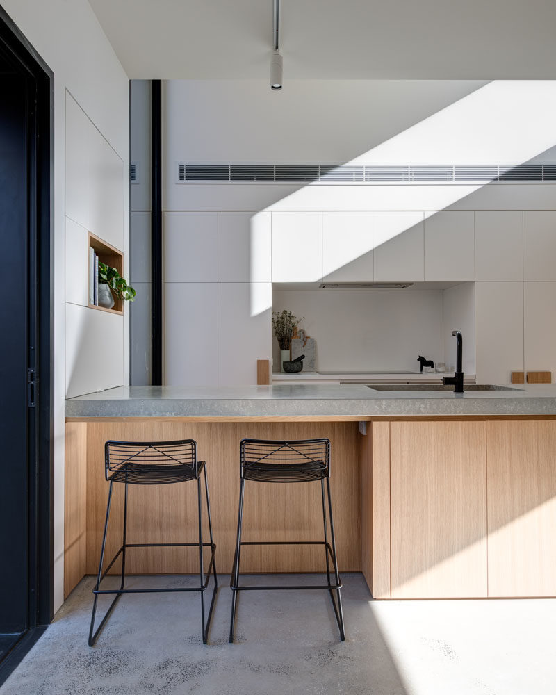 Kitchen Ideas - This modern kitchen has a large wood peninsula, minimalist white cabinets, oversized hardware, and built-in wine storage. Behind the kitchen is a door that leads to the laundry room. #KitchenIdeas #ModernKitchen #KitchenDesign