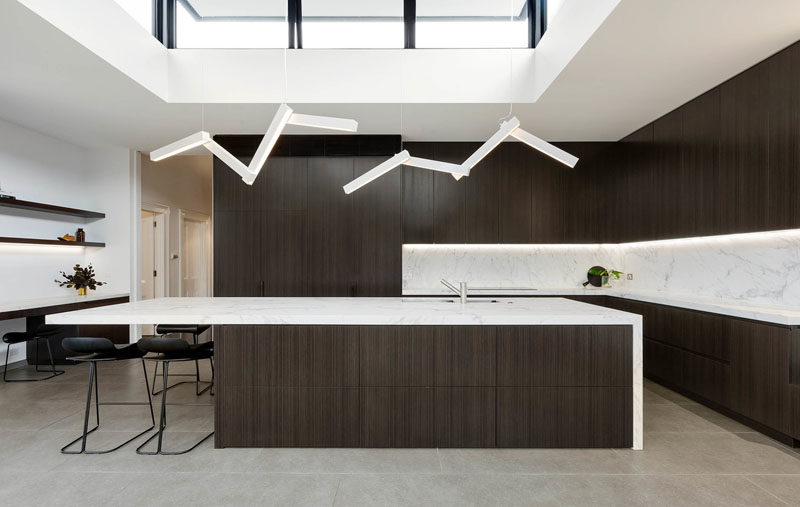 Kitchen Ideas - This modern kitchen has dark wood cabinets with light countertops, while a pair of lights draws the eye upwards to the clerestory windows. #KitchenIdeas #DarkKitchen #WoodKitchen #Windows