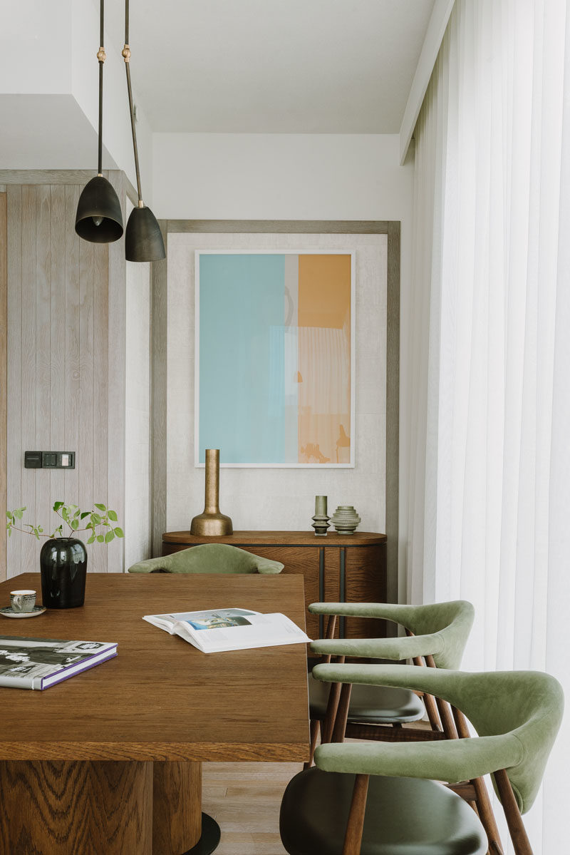 Dining Room Ideas - A large wood table is surrounded by soft green and wood chairs, while abstract wall art hangs above a small sideboard. #DiningRoomIdeas #DiningRoom