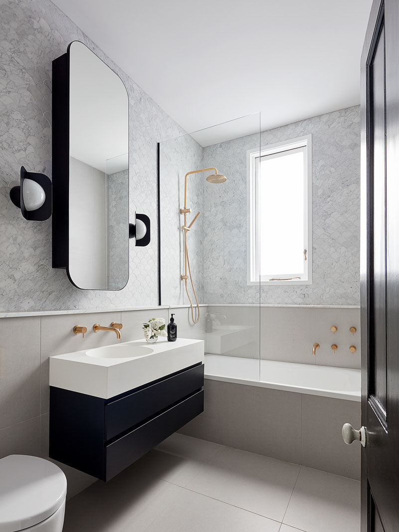 Bathroom Ideas - In this modern bathroom, a rounded rectangular mirror hangs above a small black and white vanity, while the black sconces complement the lower section of the vanity. Touches of gold add a glamorous touch to the space. #BathroomIdeas #ModernBathroom