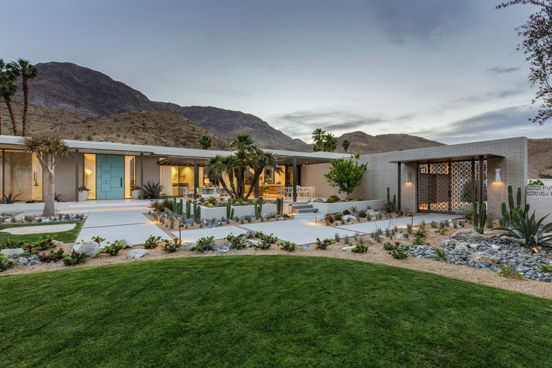 The exterior of this renovated mid-century modern house features brick, stucco, painted steel, and glass, while the exterior walkways are made from poured concrete. #RenovatedHouse #LandscapeDesign #Landscaping