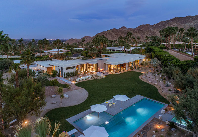 The rear of this modern house opens to a large yard, with a lawn, a swimming pool, and numerous outdoor living areas. #Landscaping #Yard #ModernPool #Garden