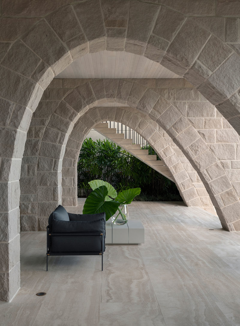 On the ground floor of this modern house, sandstone arches, lined timber ceiling boards, and travertine flooring form a powerful, tough, and muscular base to the home. #SandstoneArches #ModernHouse #ModernArchitecture #TravertineFlooring