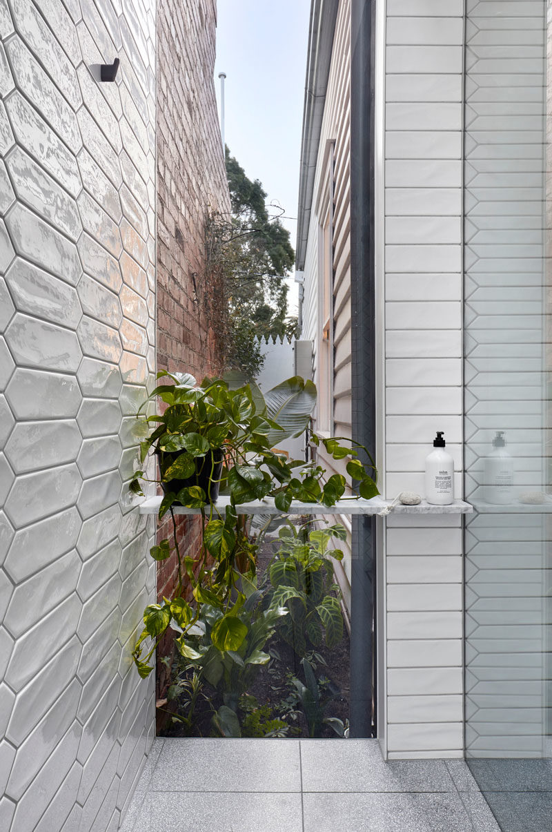 Bathroom Ideas - In this modern white bathroom,  white picket tiles cover the walls, and in the shower, a floor-to-ceiling window with views of a tiny garden at the side of the house. #BathroomIdeas #PicketTiles #WhiteTiles #Windows