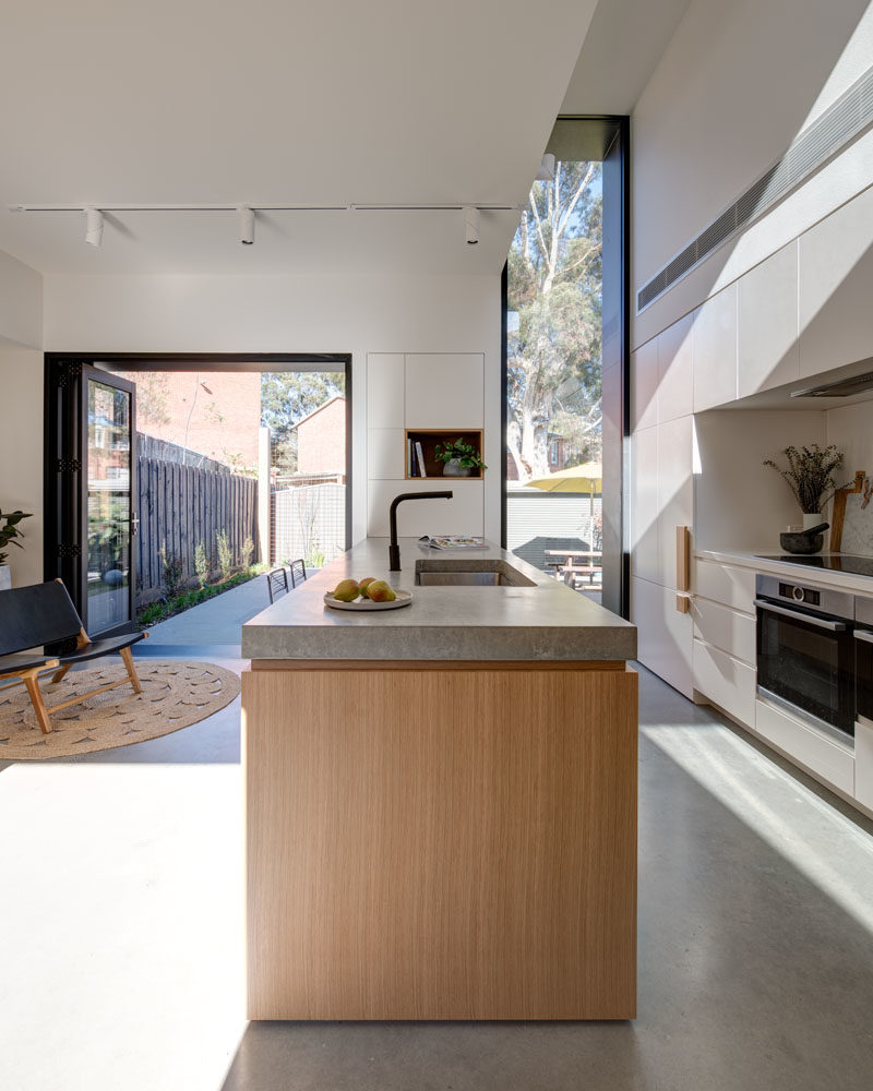 Kitchen Ideas - This modern kitchen has a large wood peninsula, minimalist white cabinets, oversized hardware, and built-in wine storage. Behind the kitchen is a door that leads to the laundry room. #KitchenIdeas #ModernKitchen #KitchenDesign