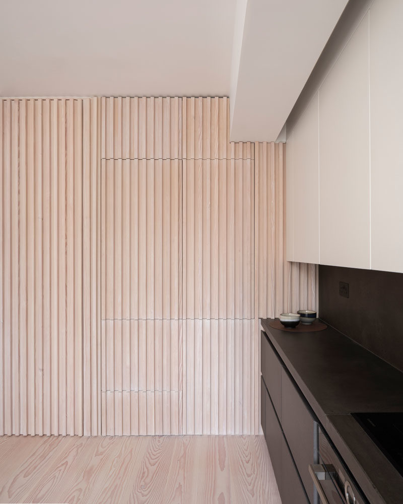 Interior Design Ideas - The wood slat wall in this modern apartment incorporates secret doors, and all storage and service requirements for the apartment, including kitchen appliances and hanging cupboards, resulting in a highly efficient plan. #InteriorDesignIdeas #WoodSlatWall #HiddenAppliances #HiddenFridge #IntegratedFridge #HiddenStorage #SecretDoors #HiddenDoors