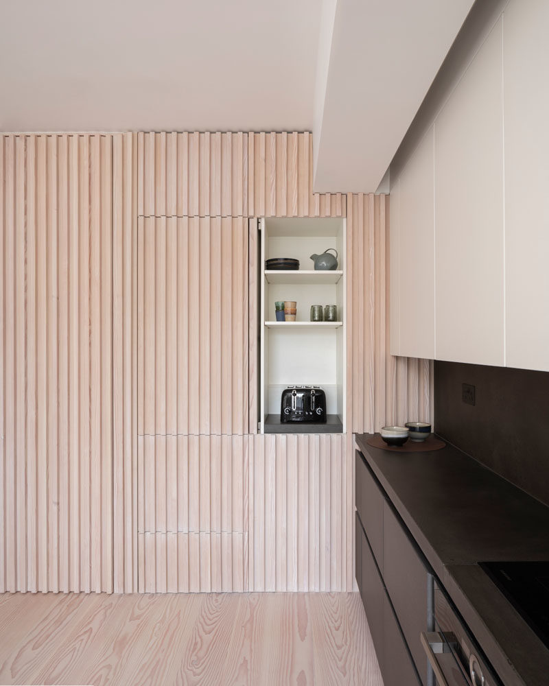 Interior Design Ideas - The wood slat wall in this modern apartment incorporates secret doors, and all storage and service requirements for the apartment, including kitchen appliances and hanging cupboards, resulting in a highly efficient plan. #InteriorDesignIdeas #WoodSlatWall #HiddenAppliances #HiddenFridge #IntegratedFridge #HiddenStorage #SecretDoors #HiddenDoors