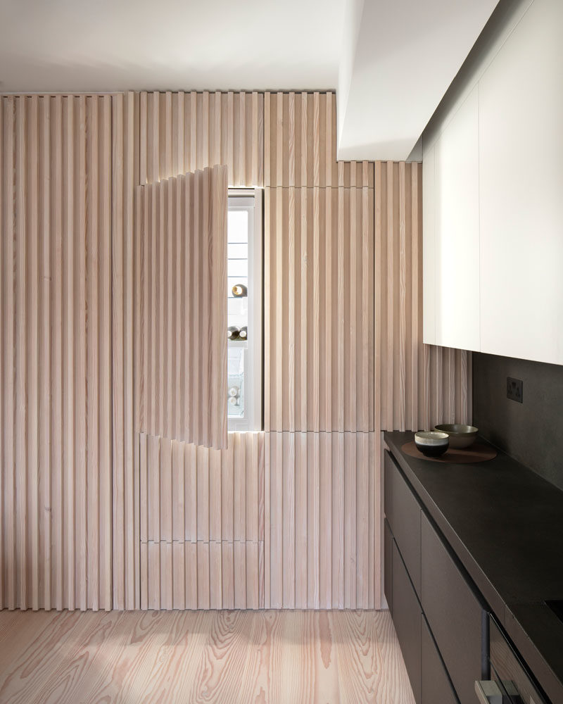 Interior Design Ideas - The wood slat wall in this modern apartment incorporates secret doors, and all storage and service requirements for the apartment, including kitchen appliances and hanging cupboards, resulting in a highly efficient plan. #InteriorDesignIdeas #WoodSlatWall #HiddenAppliances #HiddenFridge #IntegratedFridge #HiddenStorage #SecretDoors #HiddenDoors