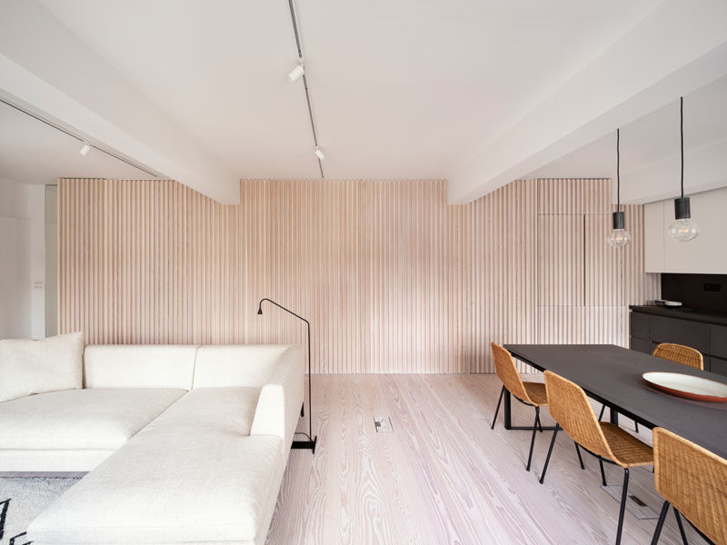 Interior Design Ideas - The wood slat wall in this modern apartment incorporates secret doors, and all storage and service requirements for the apartment, including kitchen appliances and hanging cupboards, resulting in a highly efficient plan. #InteriorDesignIdeas #WoodSlatWall #HiddenAppliances #HiddenFridge #IntegratedFridge #HiddenStorage #SecretDoors #HiddenDoors