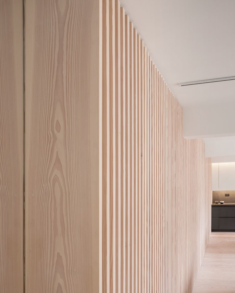 Interior Design Ideas - The wood slat wall in this modern apartment incorporates secret doors, and all storage and service requirements for the apartment, including kitchen appliances and hanging cupboards, resulting in a highly efficient plan. #InteriorDesignIdeas #WoodSlatWall #HiddenAppliances #HiddenFridge #IntegratedFridge #HiddenStorage #SecretDoors #HiddenDoors