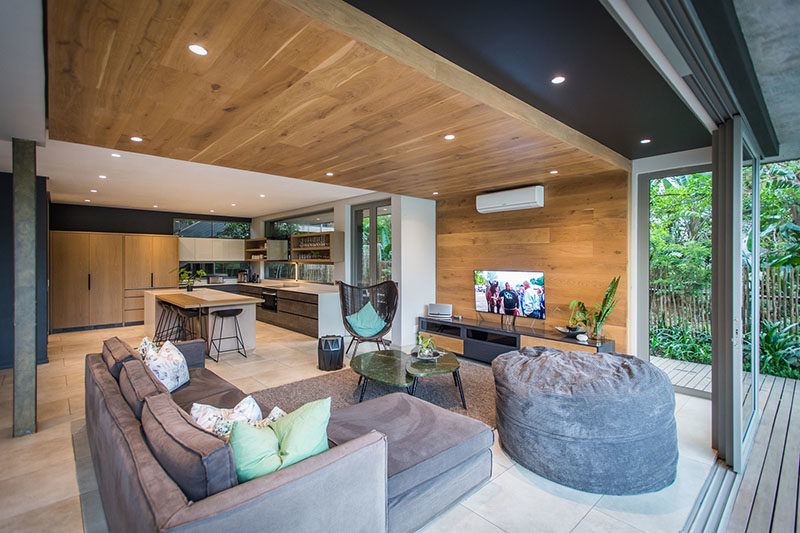 LIVING ROOM IDEAS - One of the most eye-catching design elements of this modern interior by Metropole Architects, was the inclusion of a wrap-around wood accent wall in the living room that travels from the wall up onto the ceiling. #LivingRoom #WoodAccentWall #WoodCeiling #InteriorDesign #AccentWall #LivingRoomIdeas