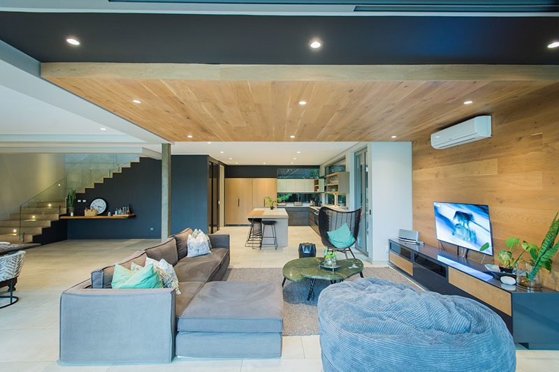 LIVING ROOM IDEAS - One of the most eye-catching design elements of this modern interior by Metropole Architects, was the inclusion of a wrap-around wood accent wall in the living room that travels from the wall up onto the ceiling. #LivingRoom #WoodAccentWall #WoodCeiling #InteriorDesign #AccentWall #LivingRoomIdeas