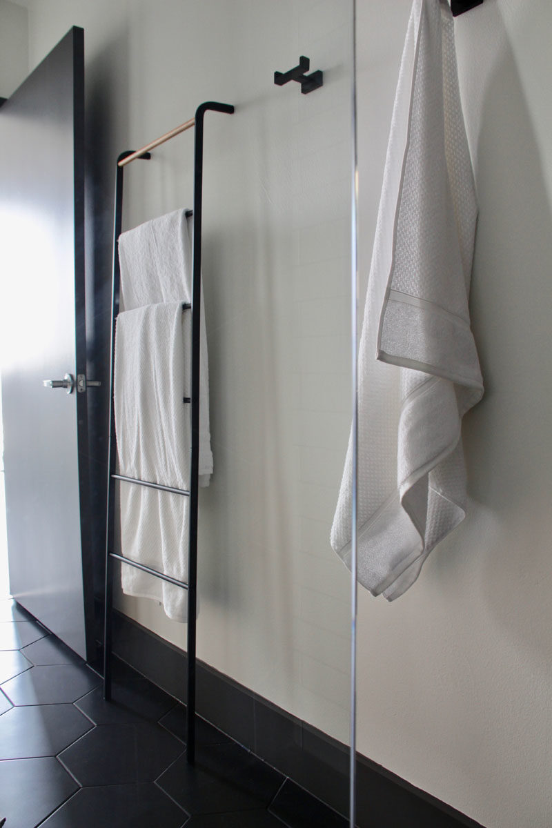 In this modern bathroom, black hooks and a towel rack create a space to hang towels and clothes. #BathroomDesign #BathroomHooks #TowelRack