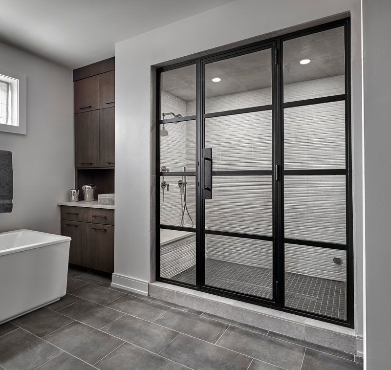 Shower Ideas - In this modern master bathroom, the walk-in shower is enclosed behind a blackened steel and glass door. Inside the shower, large format striated wall tile has been combined with a black mosaic shower floor tile for a modern industrial look. #ShowerIdeas #ModernShower #ShowerDesign