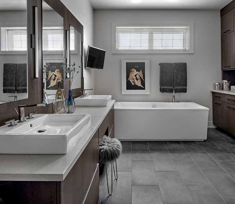 Bathroom Ideas - In this master bathroom, a custom wall hung vanity and back panel has been made from rift cut white oak with an espresso stain, while an engineered quartz counter is complemented by faucets with a titanium finish, and gray porcelain tiles cover the floor. #ModernBathroom #BathroomIdeas #DarkWoodVanity #MasterBathroom