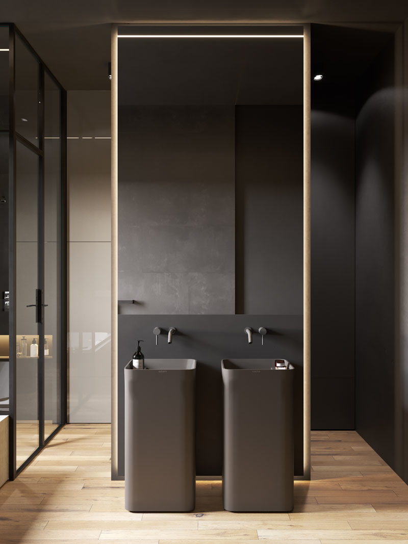 Bathroom Ideas - In this modern bathroom, two black pedestal sinks are located below a mirror, the white bath is built-in and contrasts the rest of the room, and the shower is enclosed by glass and has a built-in shelf with lighting. #BathroomIdeas #ModernBathroom #BahroomDesign #DarkBathroom