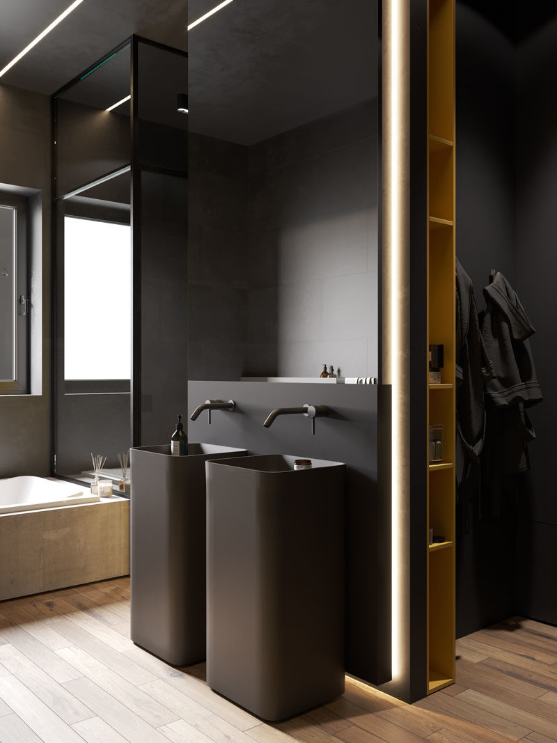 Bathroom Ideas - In this modern bathroom, two black pedestal sinks are located below a mirror, the white bath is built-in and contrasts the rest of the room, and the shower is enclosed by glass and has a built-in shelf with lighting. #BathroomIdeas #ModernBathroom #BahroomDesign #DarkBathroom