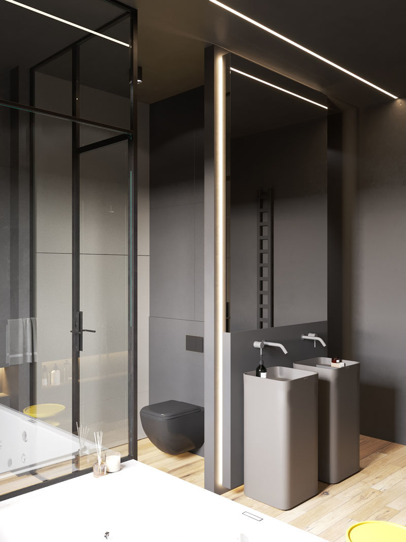 Bathroom Ideas - In this modern bathroom, two black pedestal sinks are located below a mirror, the white bath is built-in and contrasts the rest of the room, and the shower is enclosed by glass and has a built-in shelf with lighting. #BathroomIdeas #ModernBathroom #BahroomDesign #DarkBathroom