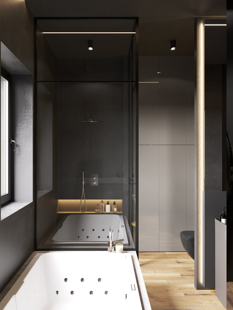 Bathroom Ideas - In this modern bathroom, two black pedestal sinks are located below a mirror, the white bath is built-in and contrasts the rest of the room, and the shower is enclosed by glass and has a built-in shelf with lighting. #BathroomIdeas #ModernBathroom #BahroomDesign #DarkBathroom