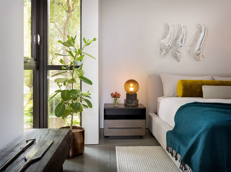 Bedroom Ideas - This modern bedroom features floor-to-ceiling windows in a corner, and a pop of color on the bed in the form of a bolster pillow and a blue throw. #BedroomIdeas #ModernBedroom #BedroomDesign