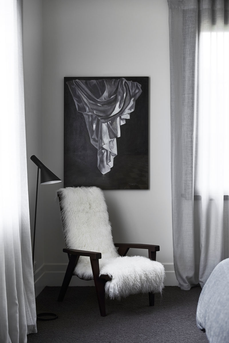 Decor Ideas - In this modern bedroom, a sheepskin is hung over an armchair providing a comfy place to relax, while wall art adds to the black, white and grey color palette. #ModernDecor #DecorIdeas #BedroomDecor