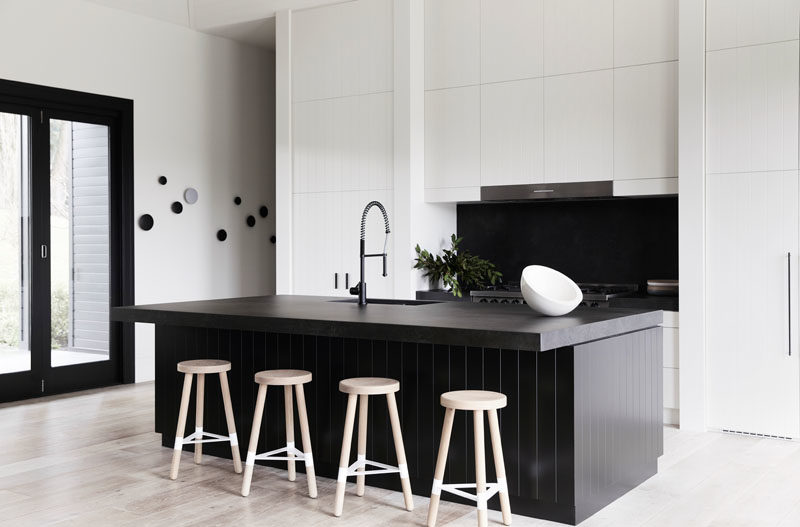 Kitchen Ideas - In this modern farmhouse kitchen, there's a new 9 foot (3m) central island with a black stone countertop and wood paneling, that also strongly contrasts the crisp white cabinets on the wall behind it. #KitchenIdeas #FarmhouseKitchen #BlackAndWhite #KitchenDesign