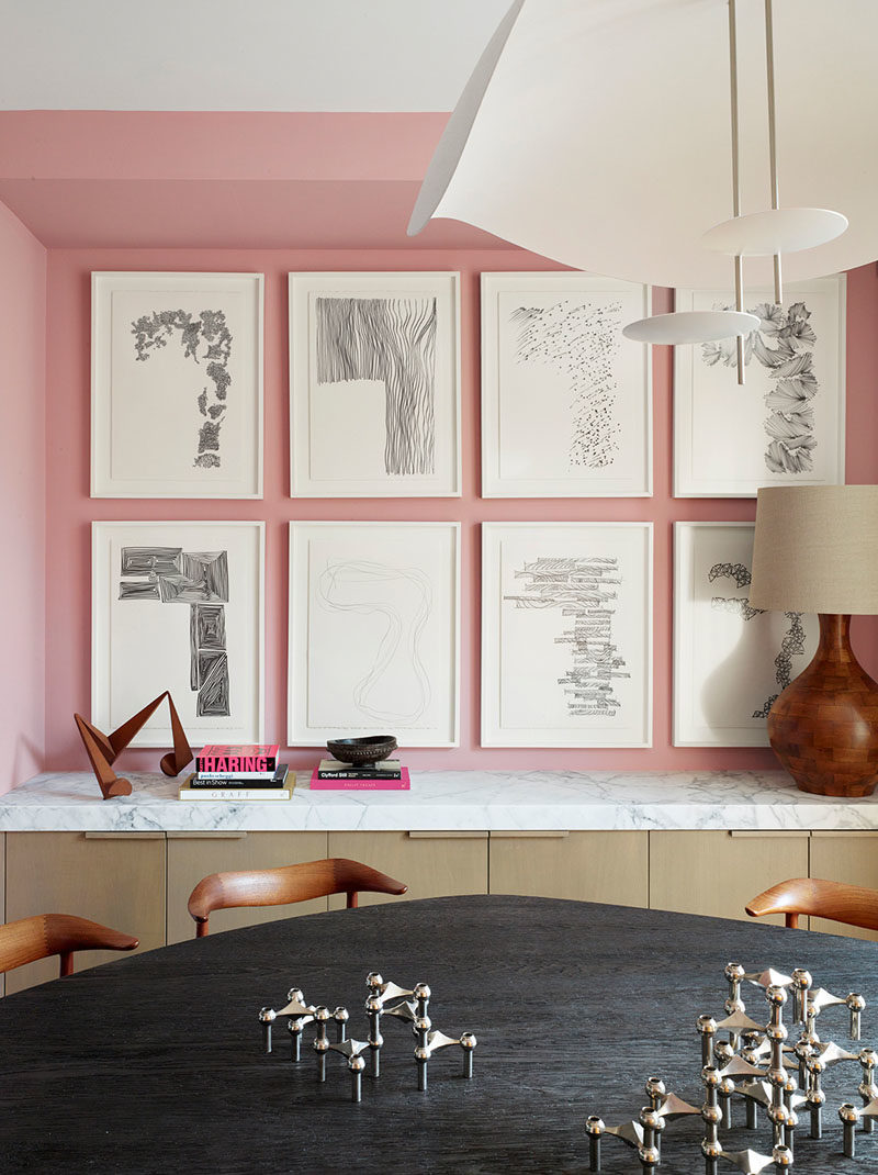 Dining Room Ideas - In this modern dining room, soft pink has been used to create a colorful backdrop for the artwork and dining table, which was designed by Jamie Bush + Co., and is shaped like an oblong pebble with a highly textured wire-brushed finish, that exposes the grain of the blackened oak. #DiningRoomIdeas #DiningRoom #PinkRoom #PinkWalls #InteriorDesign