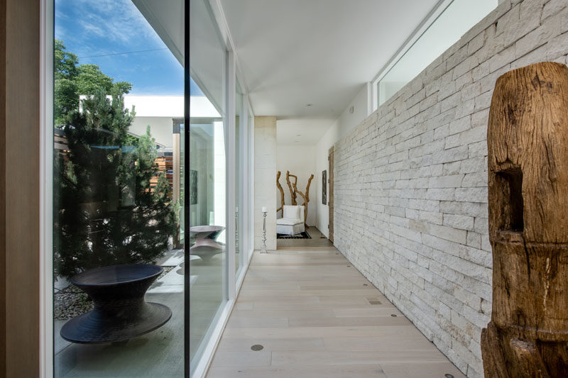 This modern hallway features a floor to ceiling glass wall and a wall of limestone. #HallwayIdeas #HallwayDesign #Windows #LimestoneWall