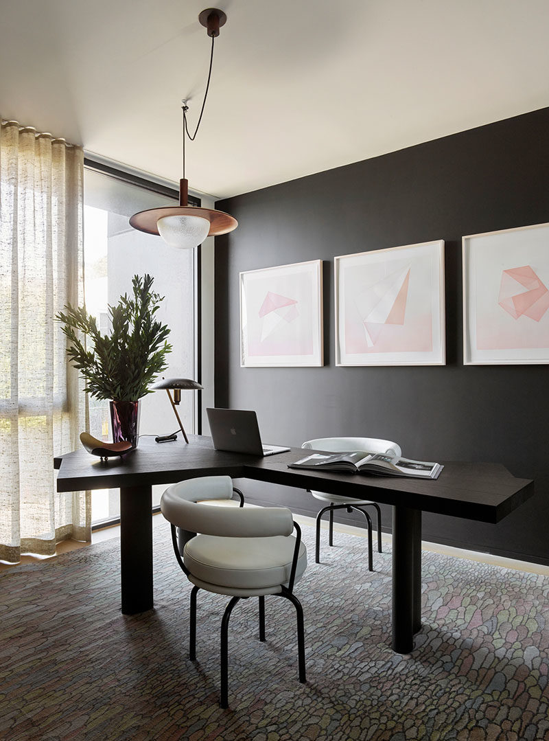 Home Office Ideas - This modern home office has a black accent wall that complements the desk, while light colored artwork and floor-to-ceiling windows helps to keep the room bright. #HomeOfficeIdeas #BlackWall #InteriorDesign