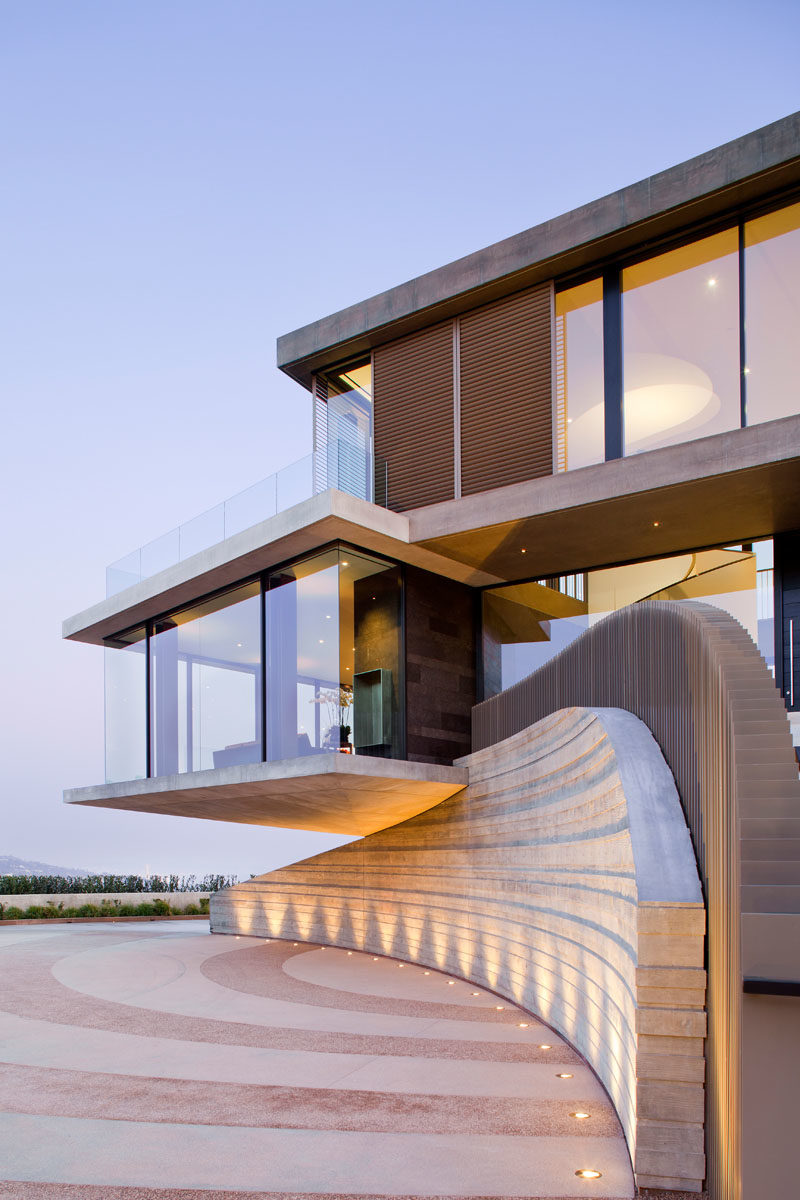 This modern house is tucked into the hillside highlighting the natural contours of the land, while a motor court has been given a decorative pattern, and well-lit stairs lead to the front door. #HouseDesign #ModernHouse #ModernArchitecture