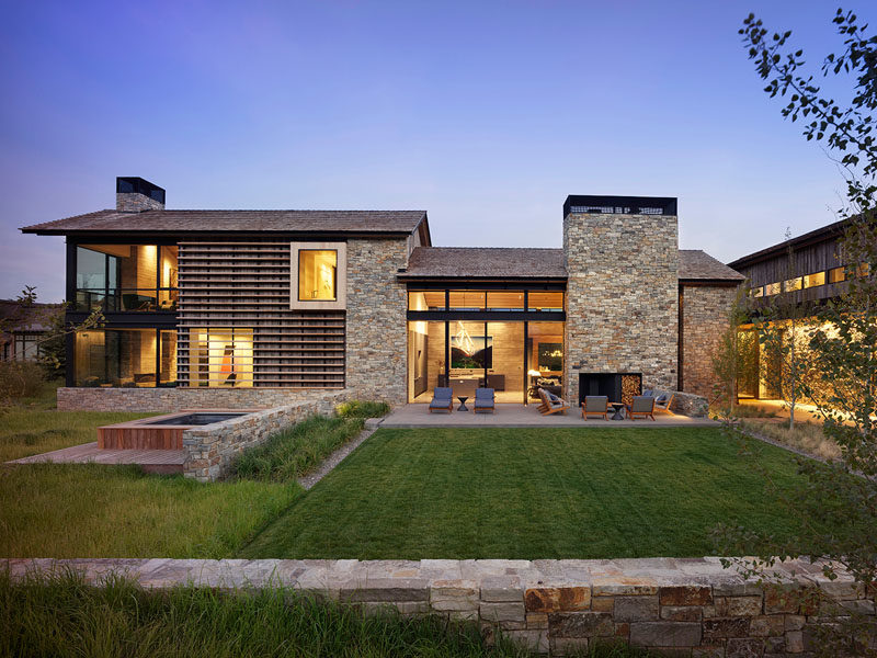 The modern house has a cedar shingle, gabled roof with eaves that extend to protect the reclaimed barn wood siding from the elements. A ribbon of rustic local fieldstone runs the perimeter of the project’s base and also clads the chimneys and feature walls. #ModernHouse #HouseDesign #ModernArchitecture