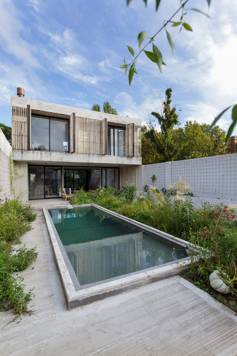 This modern house has a the furnished patio that leads to a swimming pool, as well as modern wood shutters that add a natural touch to the concrete construction of the home. #ModernShutters #ModernHouse #ConcreteHouse #SwimmingPool #Landscaping