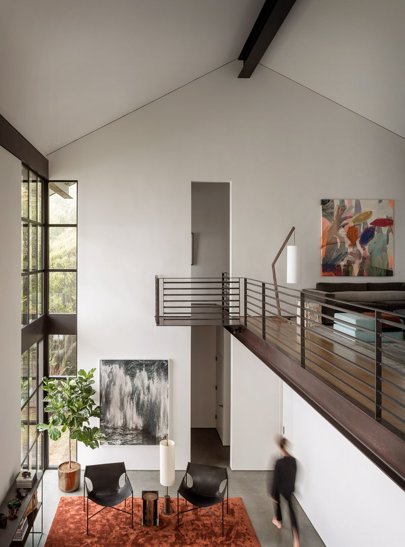 In this modern house, stairs by the front door lead to the upper floor of the home, that features a balcony overlooking the living room below. #InteriorBalcony #Architecture #HouseDesign