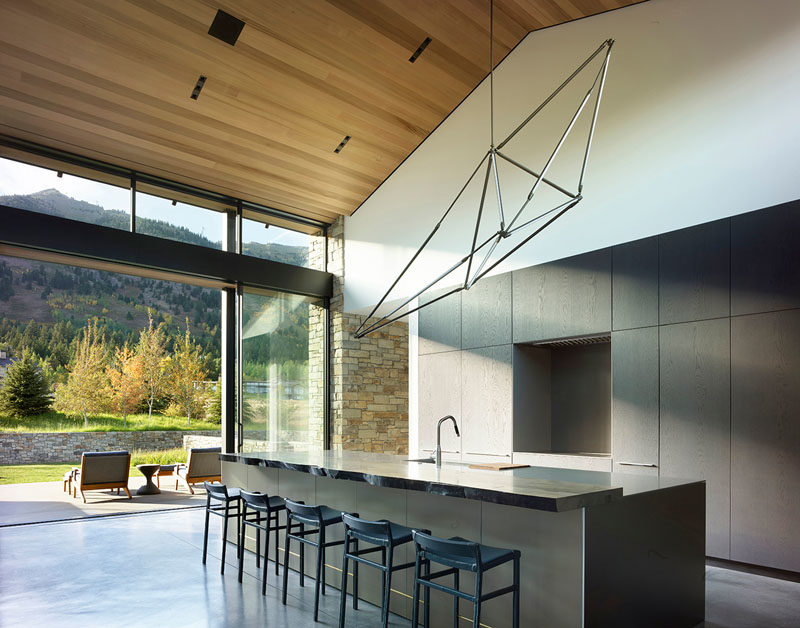 Kitchen Ideas - In this modern kitchen, minimalist dark cabinets and a large island contrast the wood ceiling and white walls. #KitchenIdeas #ModernKitchen #MinimalistKitchen