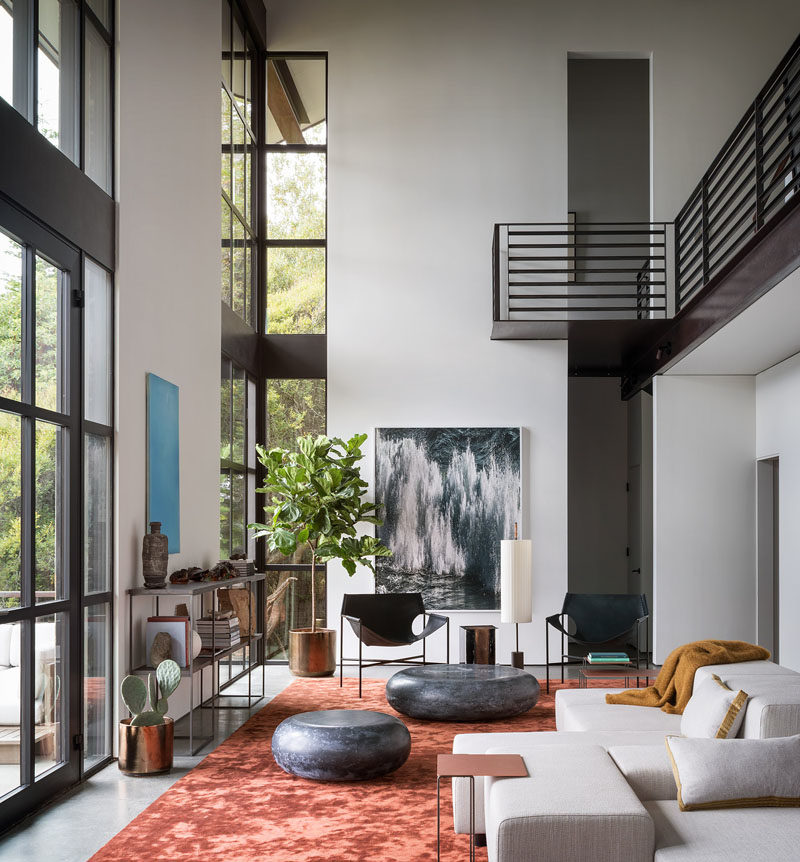 Living Room Ideas - Double height windows in this modern living room frame the picturesque bay and illuminate the silk Tai Ping rust carpet, while the Laurier Blanc acrylic glass Hekla Side Table & Stool, complement the Taylor Forest club chair, that sits beneath the Amir Zaki waterfall photograph. #LivingRoomIdeas #InteriorDesign #LivingRoom #ModernInterior