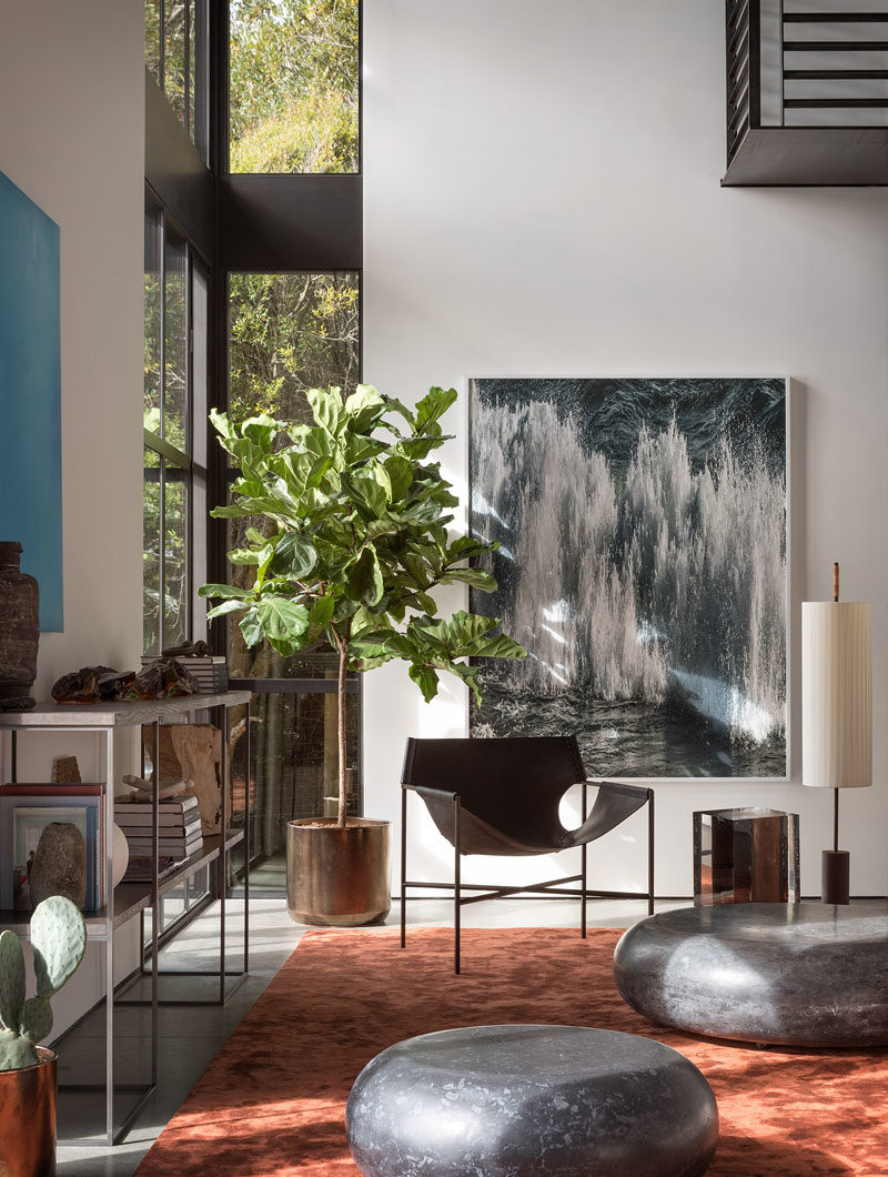 Living Room Ideas - Double height windows in this modern living room frame the picturesque bay and illuminate the silk Tai Ping rust carpet, while the Laurier Blanc acrylic glass Hekla Side Table & Stool, complement the Taylor Forest club chair, that sits beneath the Amir Zaki waterfall photograph. #LivingRoomIdeas #InteriorDesign #LivingRoom #ModernInterior