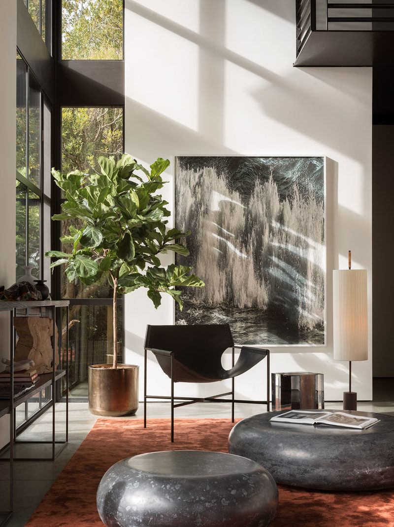 Living Room Ideas - Double height windows in this modern living room frame the picturesque bay and illuminate the silk Tai Ping rust carpet, while the Laurier Blanc acrylic glass Hekla Side Table & Stool, complement the Taylor Forest club chair, that sits beneath the Amir Zaki waterfall photograph. #LivingRoomIdeas #InteriorDesign #LivingRoom #ModernInterior